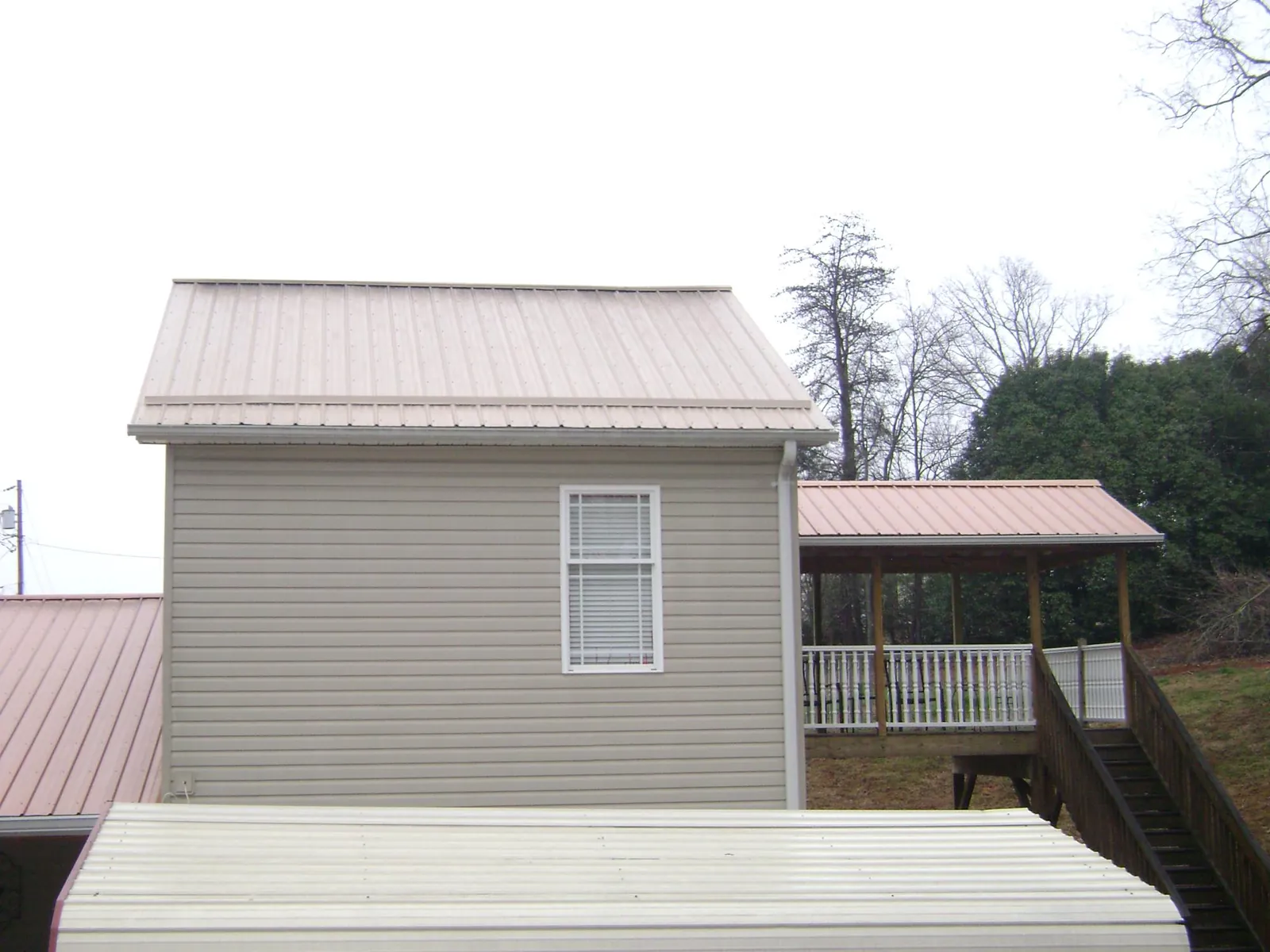 Tan metal roofs on a two story addition and attached porch, from a Roof Replacement job in Anderson